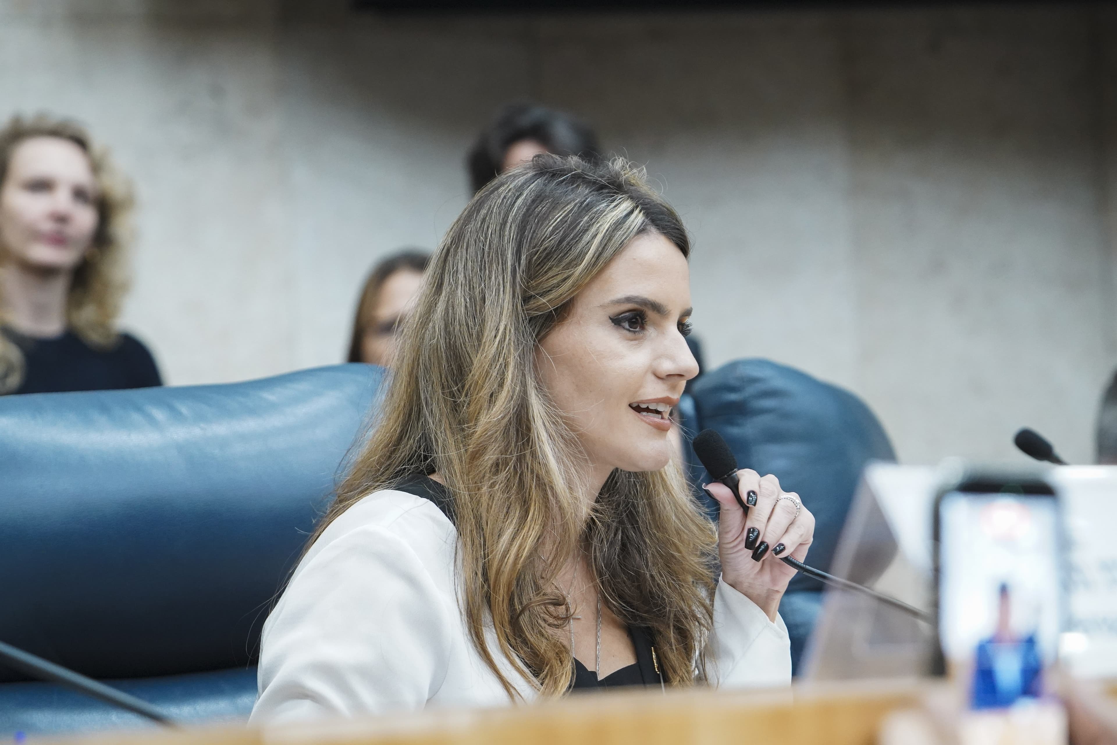 Amanda Vettorazzo, de blazer branco, fala ao microfone numa sessão