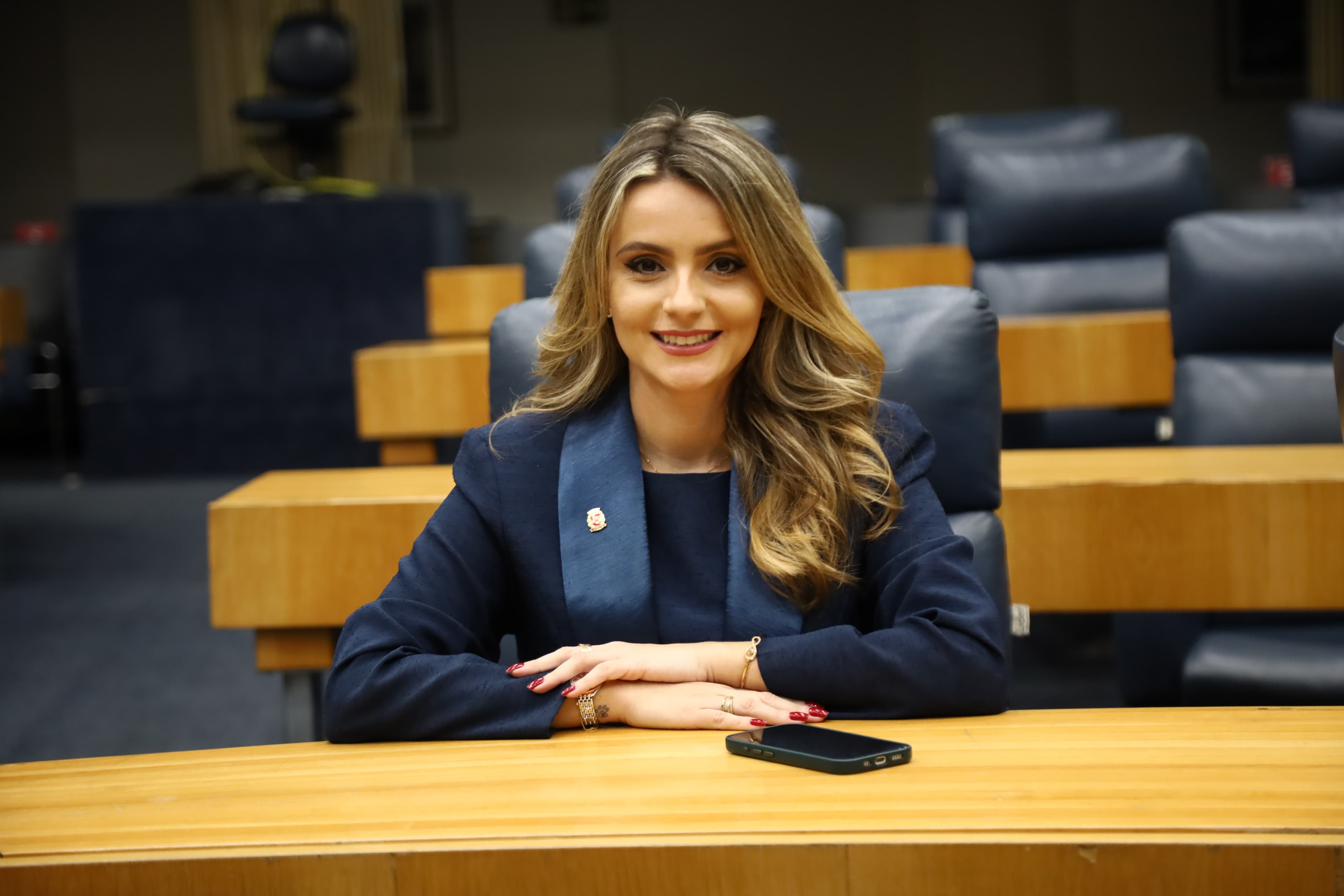 Amanda Vettorazzo sorri, sentada numa bancada do plenário da Câmara Municipal de São Paulo